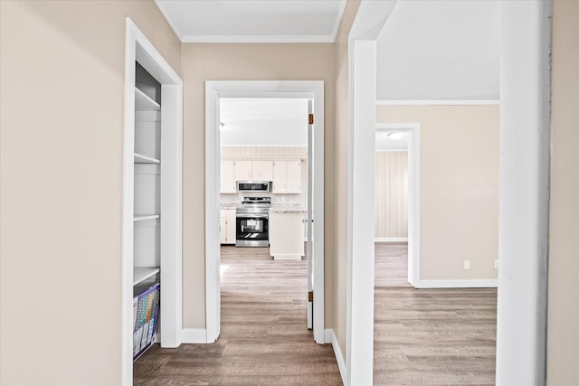 hall featuring baseboards, crown molding, and light wood-style floors