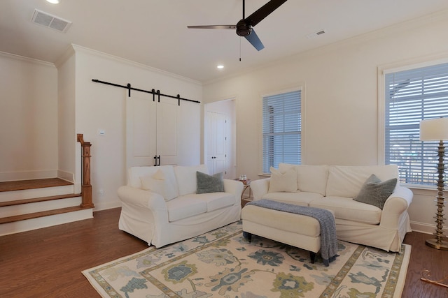 living room featuring dark hardwood / wood-style floors, ceiling fan, a barn door, and crown molding