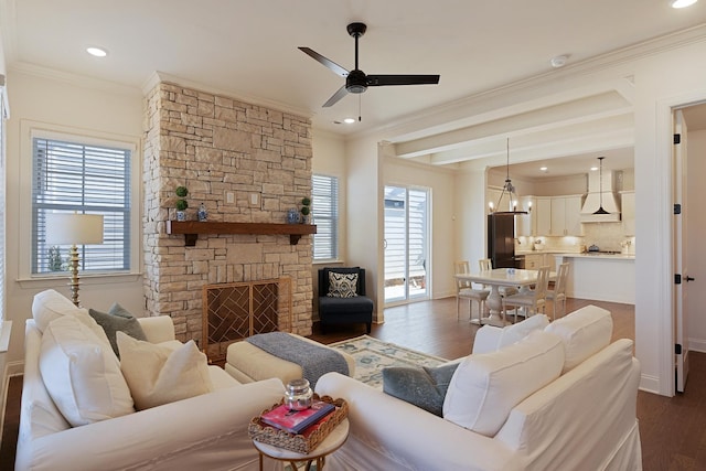 living room featuring crown molding, beam ceiling, dark hardwood / wood-style floors, a fireplace, and ceiling fan with notable chandelier