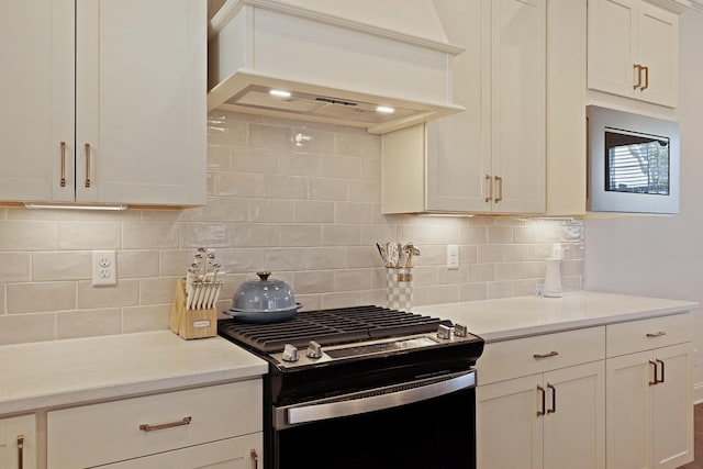 kitchen with tasteful backsplash, white cabinetry, light stone counters, gas range, and custom range hood