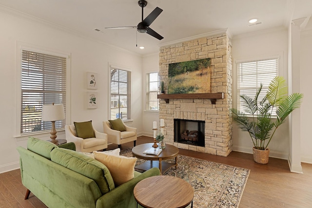 living room featuring hardwood / wood-style flooring, ornamental molding, a stone fireplace, and ceiling fan