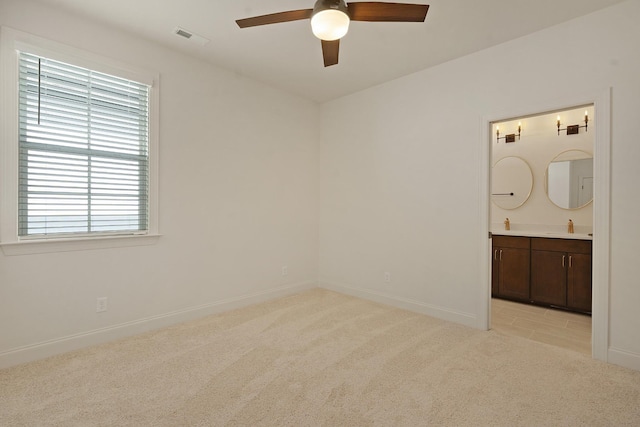 unfurnished bedroom featuring ceiling fan, sink, light carpet, and ensuite bathroom