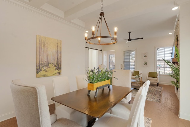 dining space with ceiling fan with notable chandelier, a barn door, light wood-type flooring, and beam ceiling