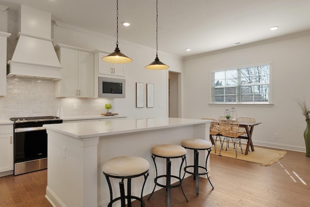 kitchen featuring stainless steel range with electric cooktop, white cabinetry, built in microwave, and a center island