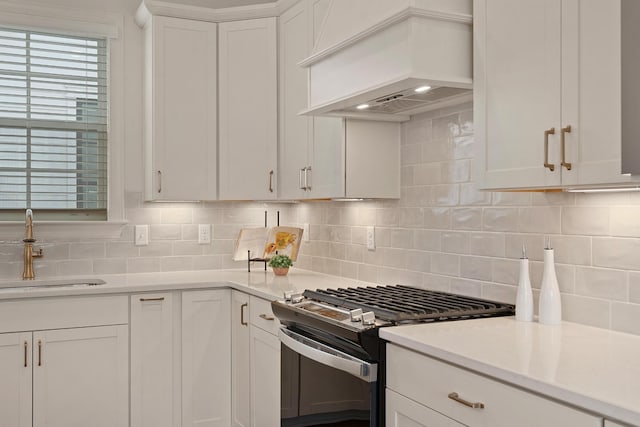 kitchen featuring white cabinetry, range with gas cooktop, premium range hood, sink, and tasteful backsplash