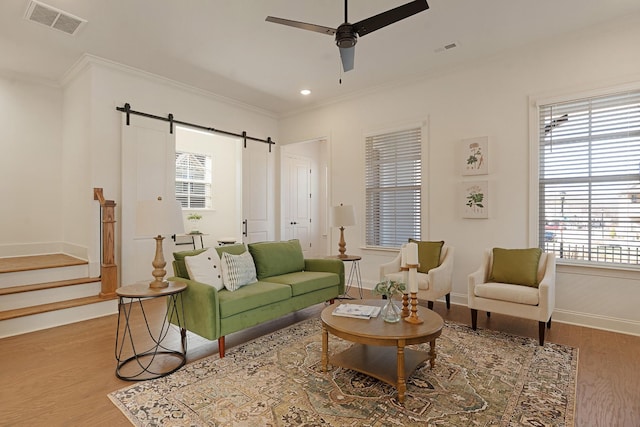 living room with hardwood / wood-style flooring, ceiling fan, a barn door, and ornamental molding