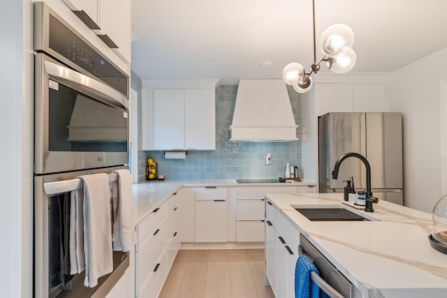 kitchen with sink, decorative light fixtures, custom range hood, stainless steel appliances, and white cabinets