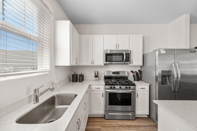 kitchen with sink, appliances with stainless steel finishes, white cabinetry, light stone counters, and light wood-type flooring