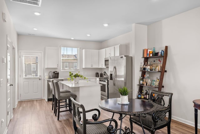 kitchen featuring white cabinetry, light hardwood / wood-style flooring, a kitchen breakfast bar, a kitchen island, and stainless steel appliances