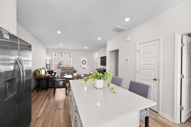 kitchen featuring a center island, stainless steel fridge, light stone countertops, light hardwood / wood-style floors, and white cabinets