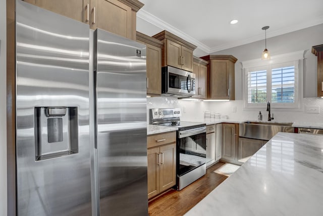 kitchen featuring appliances with stainless steel finishes, wood-type flooring, sink, hanging light fixtures, and ornamental molding