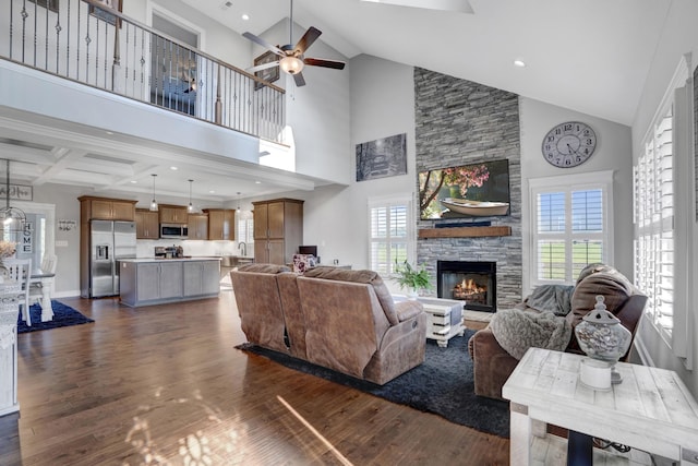 living room with a high ceiling, ceiling fan, a stone fireplace, and dark hardwood / wood-style flooring