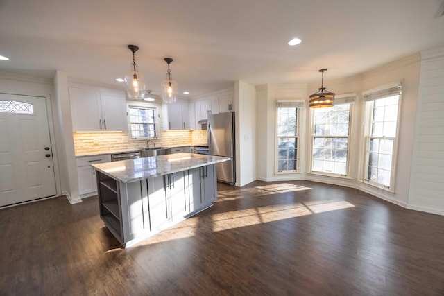 kitchen with appliances with stainless steel finishes, a kitchen island, decorative light fixtures, white cabinets, and light stone countertops