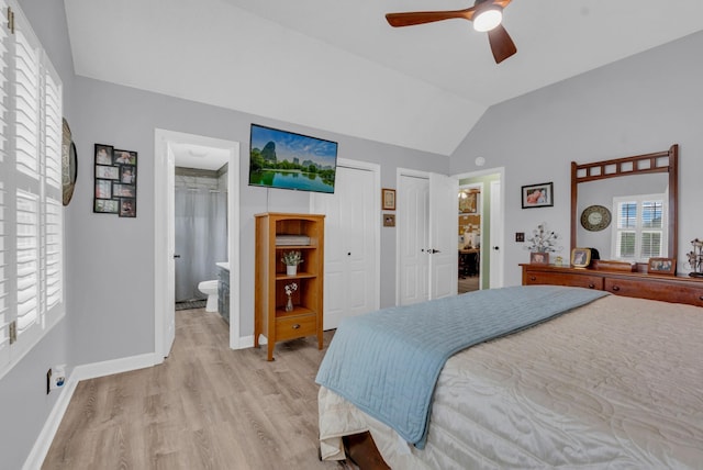 bedroom featuring ceiling fan, ensuite bathroom, two closets, vaulted ceiling, and light wood-type flooring