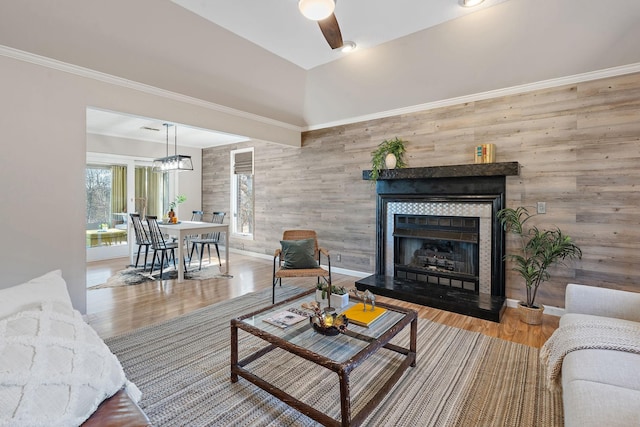 living room with wooden walls, a tiled fireplace, ornamental molding, hardwood / wood-style flooring, and ceiling fan