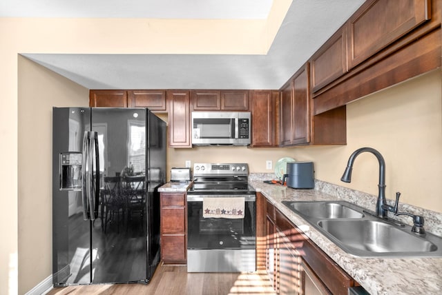 kitchen featuring stainless steel appliances, light stone countertops, sink, and light hardwood / wood-style flooring