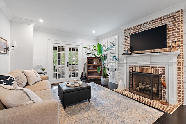 living room with a brick fireplace, crown molding, wood-type flooring, and french doors