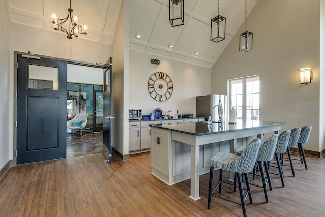 kitchen featuring hanging light fixtures, a towering ceiling, stainless steel appliances, an island with sink, and white cabinets