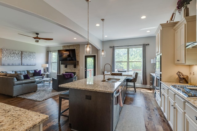 kitchen featuring a kitchen bar, sink, decorative light fixtures, light stone countertops, and a kitchen island with sink