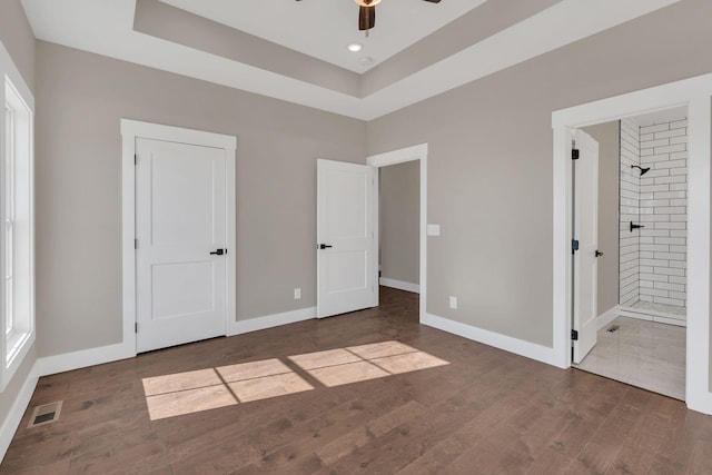 unfurnished bedroom featuring a raised ceiling, ensuite bathroom, hardwood / wood-style flooring, and ceiling fan