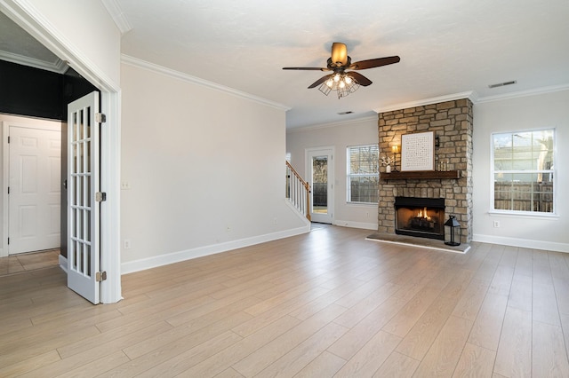 unfurnished living room with crown molding, ceiling fan, a stone fireplace, and light wood-type flooring