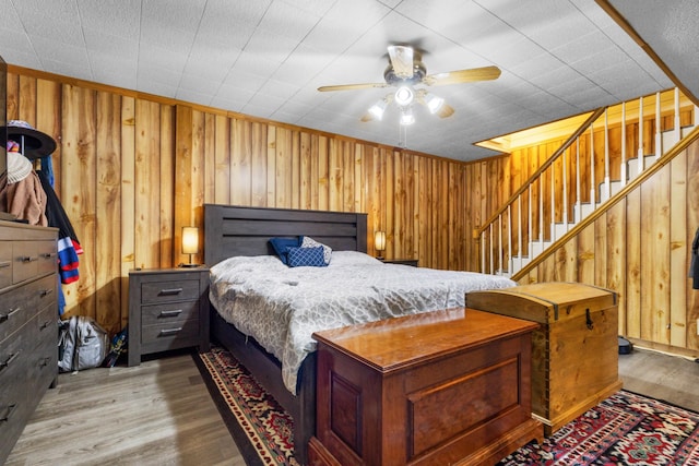 bedroom featuring ceiling fan, wooden walls, and light hardwood / wood-style floors