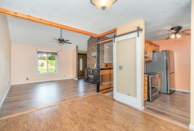 unfurnished living room with dark hardwood / wood-style flooring, lofted ceiling with beams, a barn door, and ceiling fan