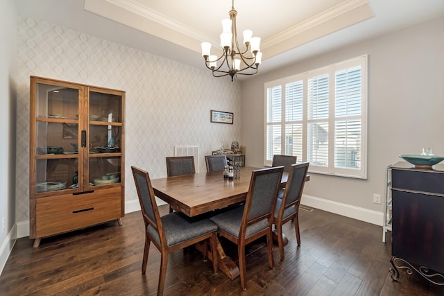 dining space with dark wood-type flooring, ornamental molding, a tray ceiling, and an inviting chandelier