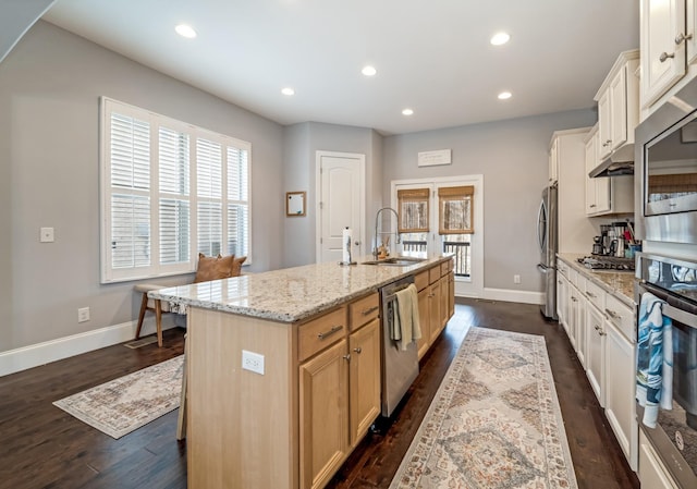 kitchen with appliances with stainless steel finishes, sink, a kitchen island with sink, light stone counters, and dark wood-type flooring