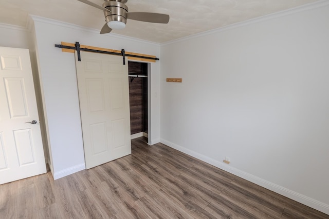 unfurnished bedroom featuring ornamental molding, a barn door, hardwood / wood-style floors, and a closet