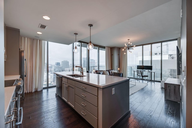 kitchen with sink, stainless steel appliances, expansive windows, an island with sink, and decorative light fixtures