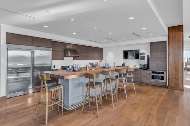 kitchen with extractor fan, a breakfast bar, wooden counters, stainless steel appliances, and dark brown cabinets