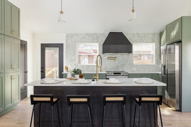 kitchen featuring an island with sink, stainless steel appliances, green cabinets, and wall chimney range hood