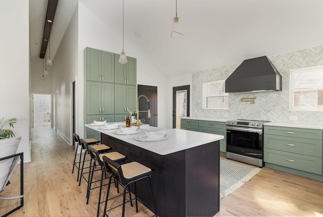 kitchen featuring high vaulted ceiling, stainless steel range with electric cooktop, a kitchen island with sink, green cabinetry, and wall chimney range hood