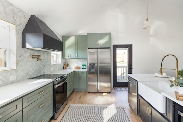 kitchen featuring appliances with stainless steel finishes, decorative light fixtures, green cabinets, and wall chimney range hood