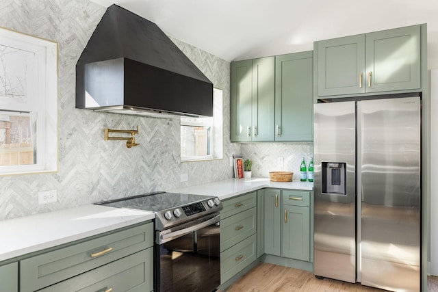 kitchen with green cabinets, stainless steel appliances, tasteful backsplash, wall chimney exhaust hood, and light wood-type flooring