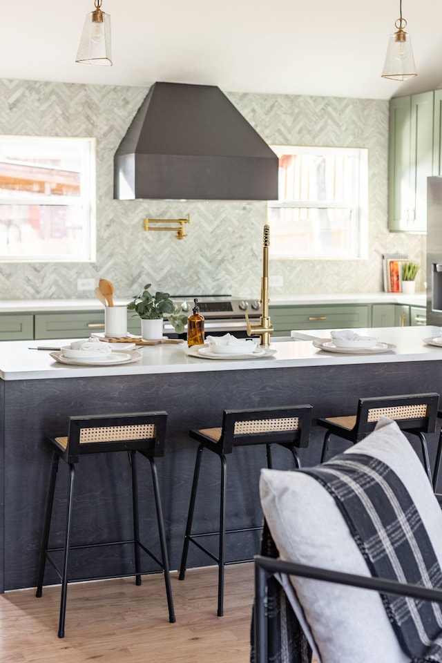 kitchen featuring a wealth of natural light, a breakfast bar area, wall chimney range hood, and green cabinetry