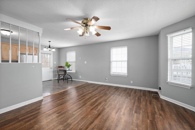 empty room featuring a textured ceiling, ceiling fan with notable chandelier, dark wood-type flooring, visible vents, and baseboards