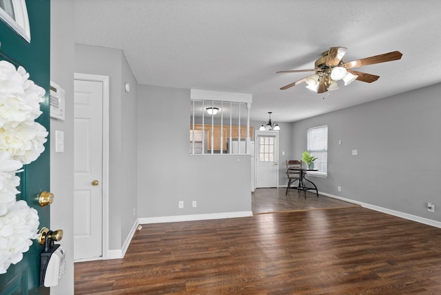 empty room featuring a textured ceiling, ceiling fan with notable chandelier, wood finished floors, and baseboards