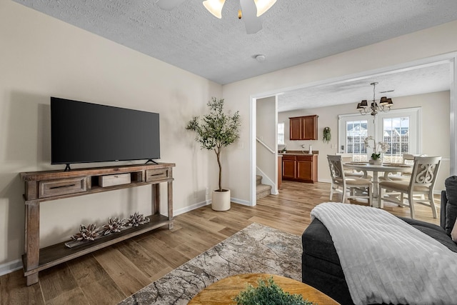 living area with ceiling fan with notable chandelier, a textured ceiling, stairway, light wood finished floors, and baseboards