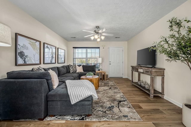 living room featuring visible vents, baseboards, wood finished floors, a textured ceiling, and a ceiling fan