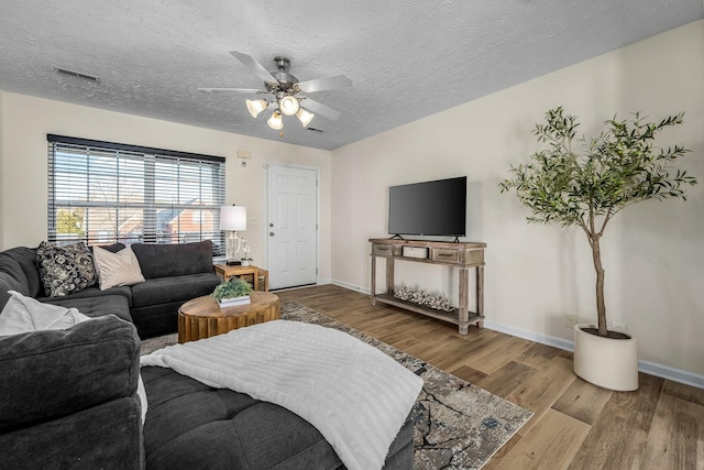 living room featuring wood finished floors, visible vents, baseboards, ceiling fan, and a textured ceiling