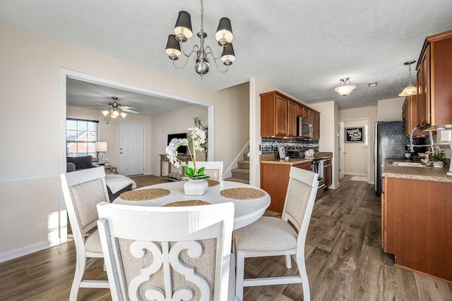 dining room with dark wood-style floors, ceiling fan with notable chandelier, a textured ceiling, and stairs