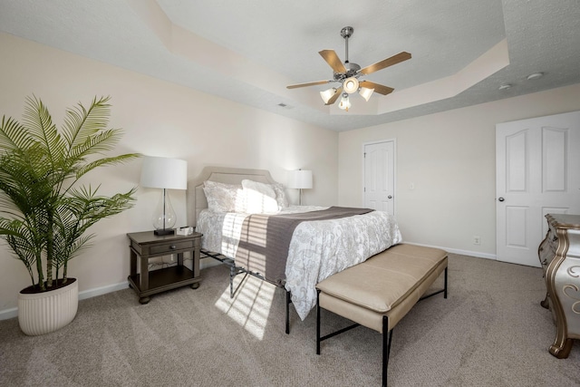 bedroom featuring a tray ceiling, a textured ceiling, carpet floors, baseboards, and ceiling fan