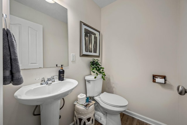 half bath with toilet, wood finished floors, and baseboards