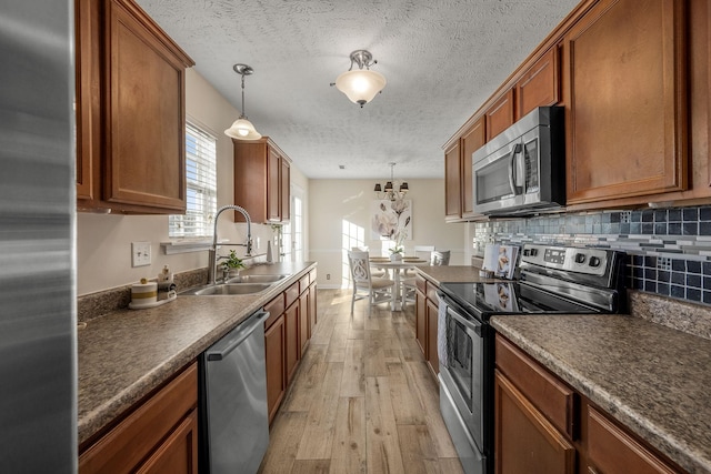 kitchen featuring sink, decorative light fixtures, light hardwood / wood-style flooring, stainless steel appliances, and decorative backsplash