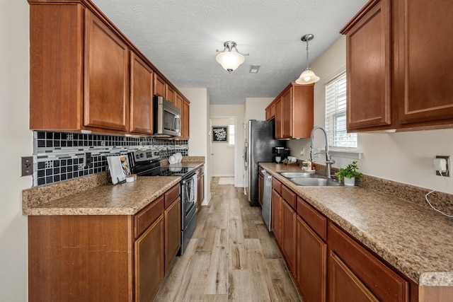 kitchen featuring brown cabinetry, a sink, decorative backsplash, appliances with stainless steel finishes, and light wood-type flooring