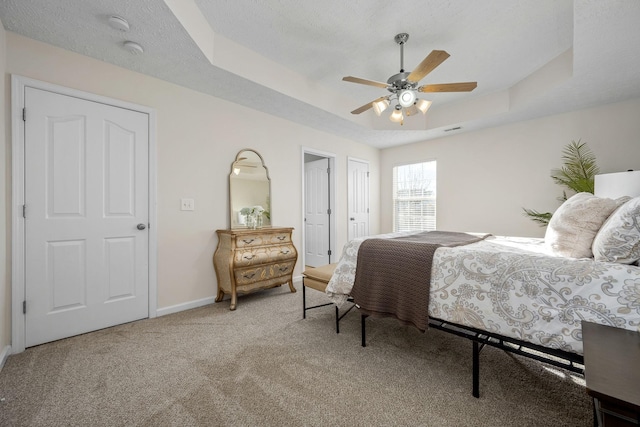 carpeted bedroom with a textured ceiling, ceiling fan, and a tray ceiling