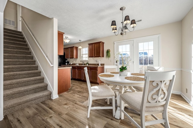 dining area featuring wood finished floors, visible vents, stairs, a textured ceiling, and a notable chandelier