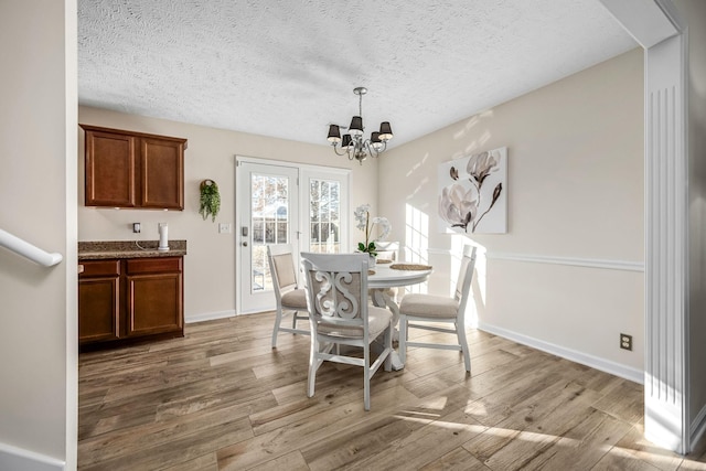 dining room with baseboards, an inviting chandelier, a textured ceiling, and light wood-style floors